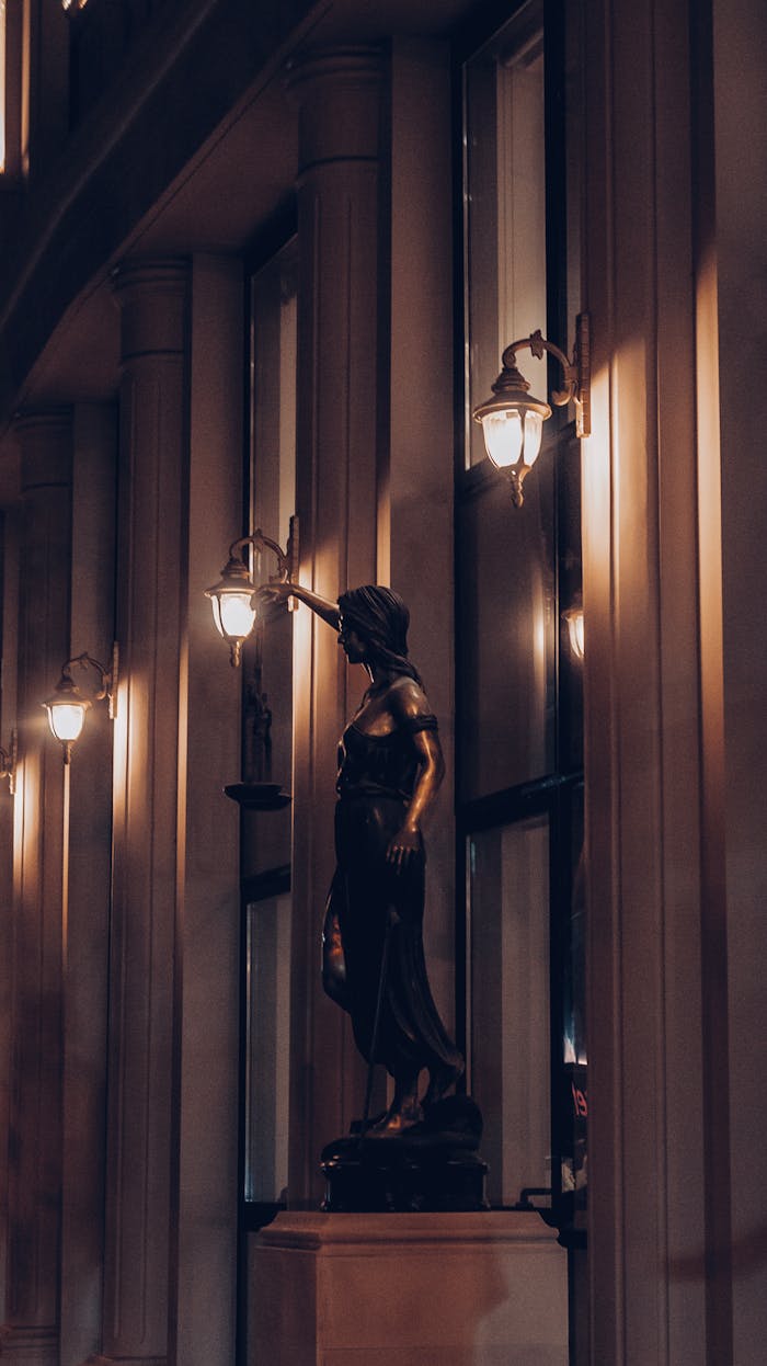 A moody evening shot of a Lady Justice statue illuminated by street lamps.