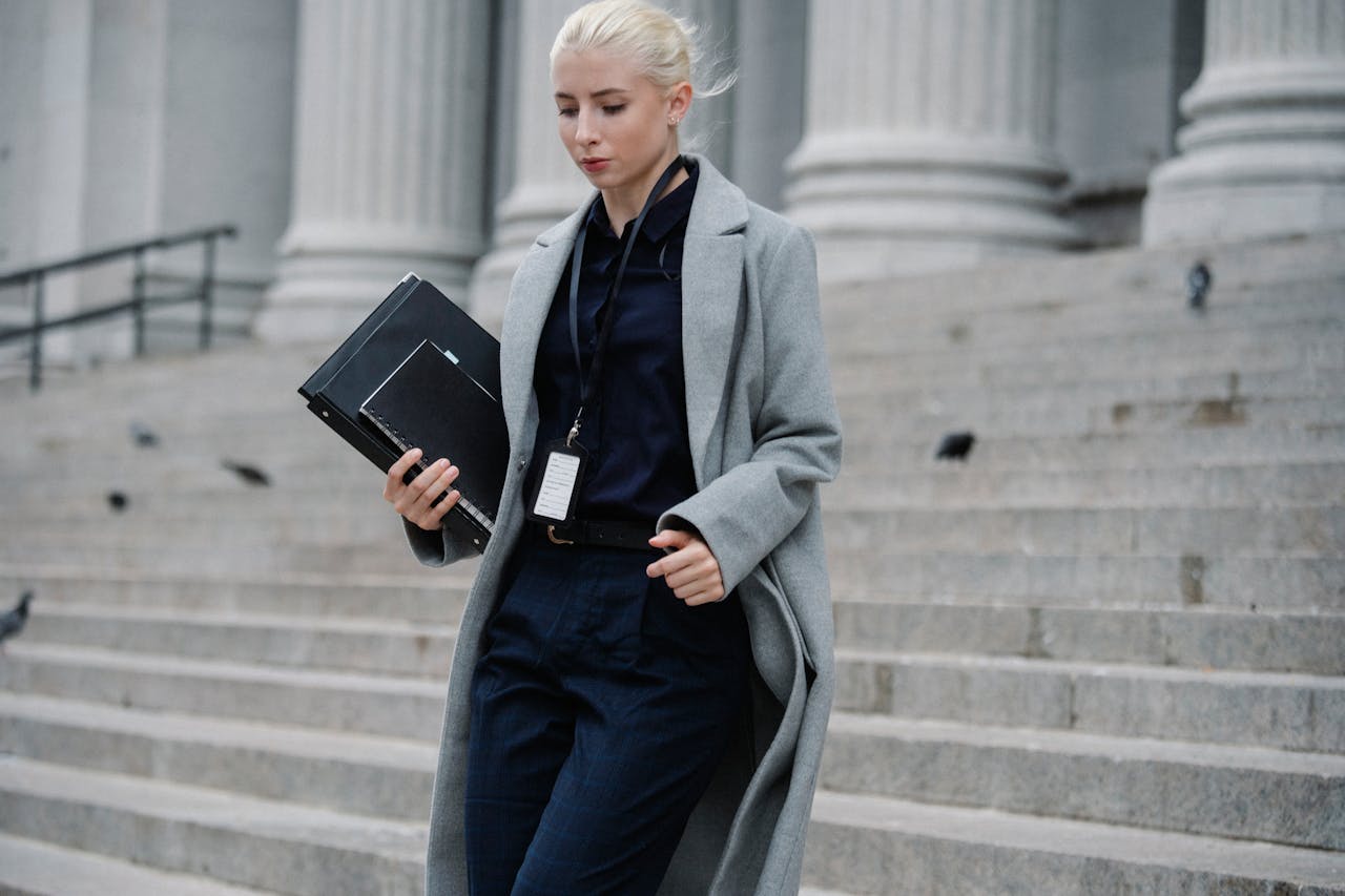Professional woman in formal attire walking down courthouse steps holding folders outdoors.
