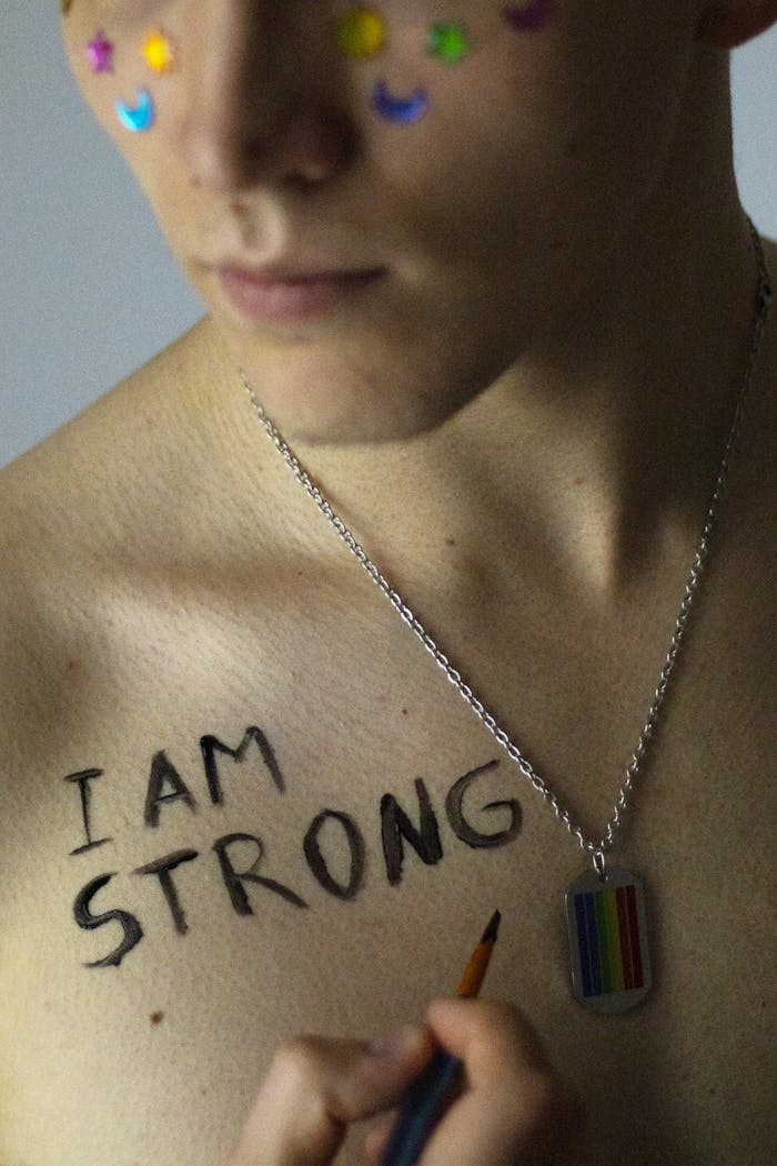 Close-up of person with 'I Am Strong' on chest and rainbow-themed necklace.