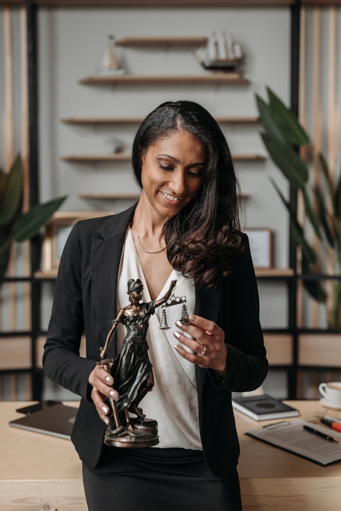 Businesswoman smiling as she holds Lady Justice figurine in modern office.