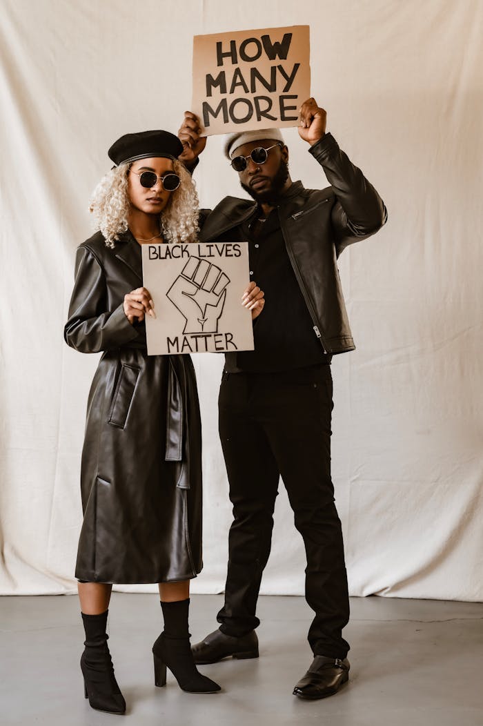Two activists in leather outfits hold Black Lives Matter protest signs indoors.